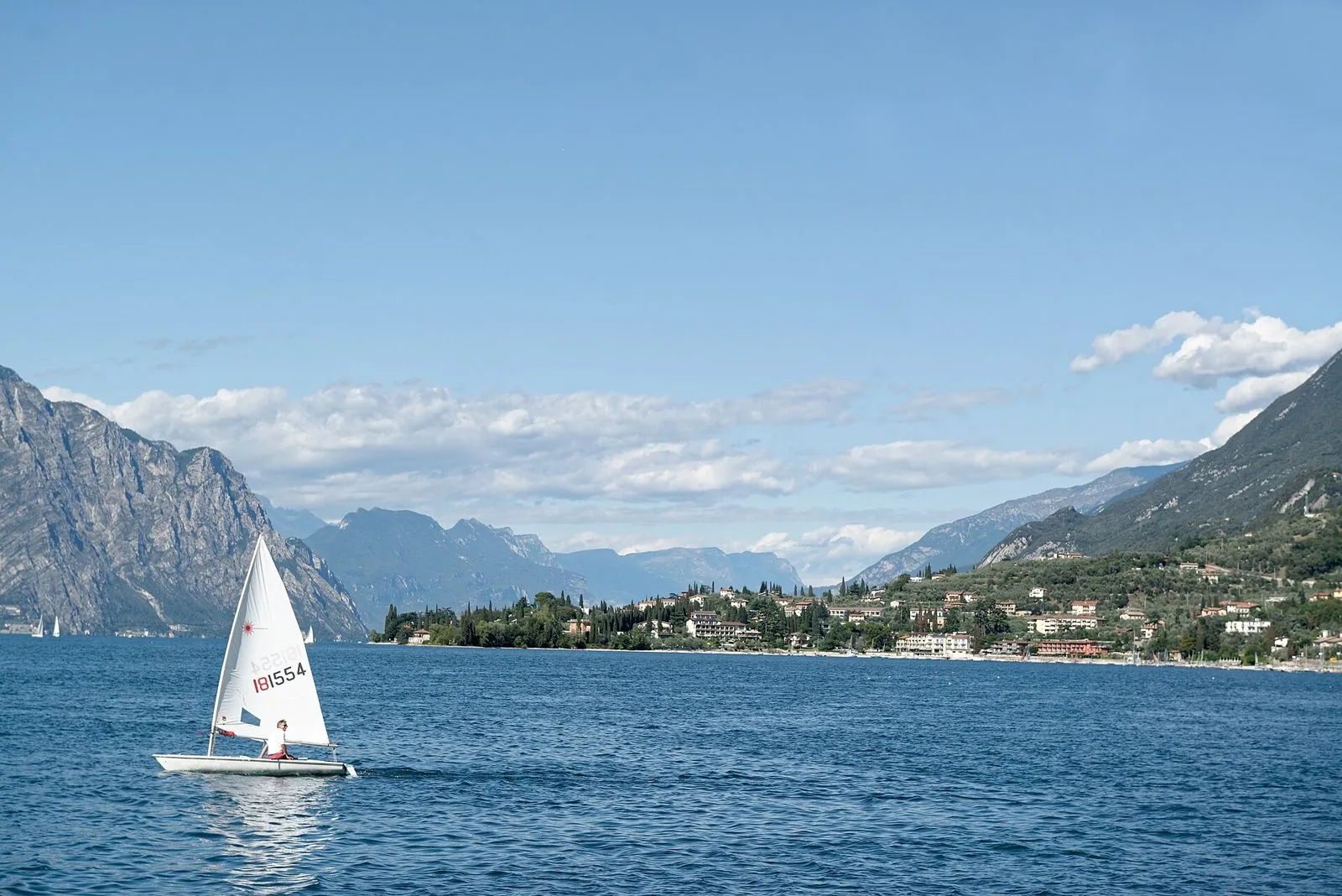 Una deriva Laser a vela sull'Alto Garda con altre vele sullo sfondo e le montagne che circondano il lago